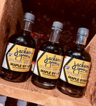 Three bottles of Jackson's General Store Golden Velvety Maple Syrup on a wooden surface.